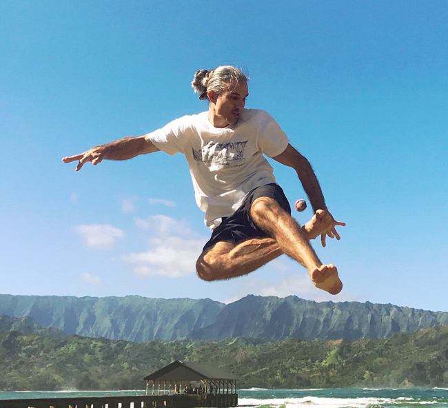 zander phelps male athlete plays hack / footbag with hackido leaping high into sky in kauai